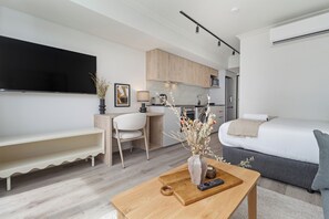 Een moderne, compacte woonruimte met een flatscreen televisie, een eethoek, een kitchenette en een bed.