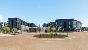 Een modern stadsplein met moderne gebouwen, een groen middelpunt en een heldere lucht.