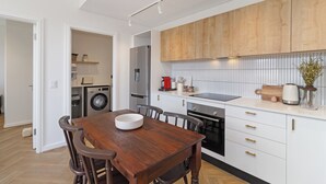 Een moderne keuken met houten kastjes, een inbouwoven en een eethoek met een houten tafel en stoelen.