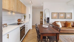 Een moderne keuken met witte kasten, een houten eettafel en een bruine leren bank in de woonkamer.
