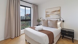 Een moderne slaapkamer met een groot bed, een nachtkastje, een raam met gordijnen en uitzicht op de stad.