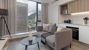 Un salon moderne avec un canapé, une petite table et une vue sur le paysage urbain, visible à travers de grandes fenêtres.
