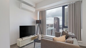 Une chambre d’hôtel moderne dotée d’un grand téléviseur à écran plat, d’un canapé, d’une petite table d’appoint et d’une fenêtre avec des rideaux.