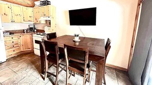 Une cuisine avec des meubles en bois, une table à manger avec des chaises et un téléviseur à écran plat fixé au mur.