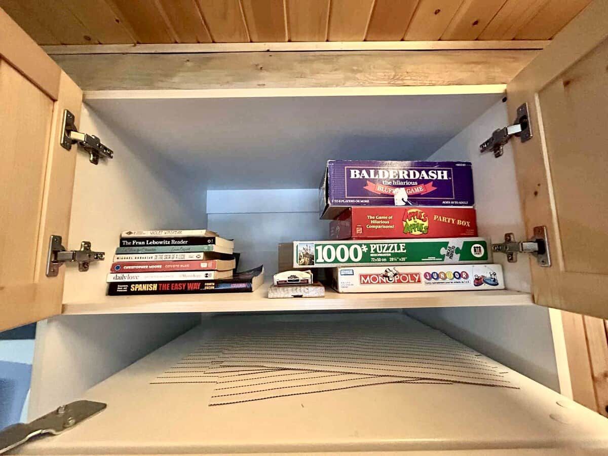 Un meuble en bois doté d’étagères où sont rangés des livres et une boîte de jeux de puzzle.