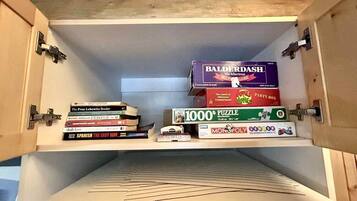 Un meuble en bois doté d’étagères où sont rangés des livres et une boîte de jeux de puzzle.