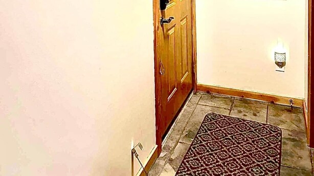 Un couloir avec une porte en bois, un porte-manteau, un tapis à motifs et un tableau représentant des skieurs.