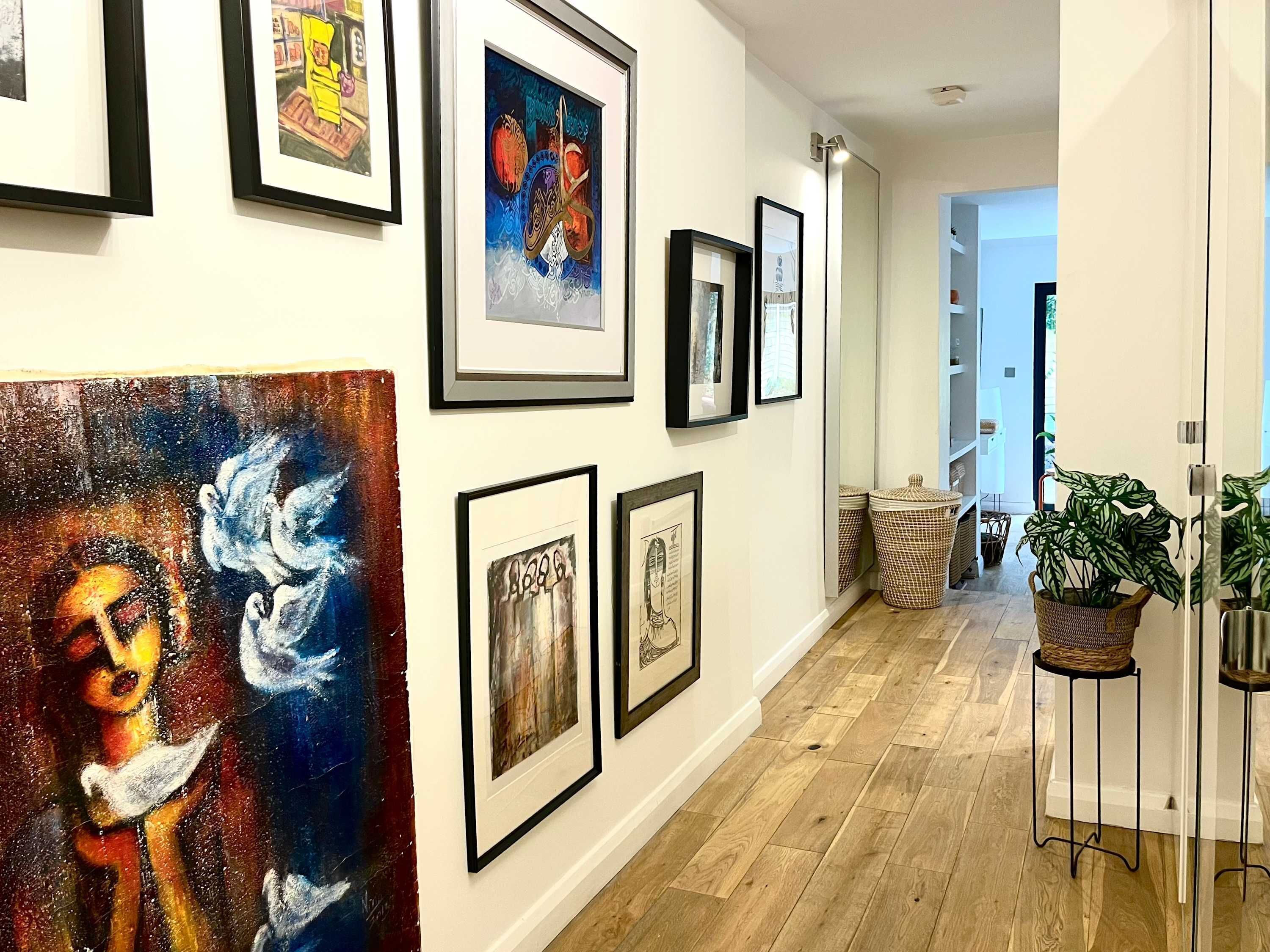 A hallway with framed artworks on the walls, wooden flooring, and potted plants.