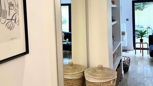 Ένας διάδρομος με έναν μεγάλο καθρέφτη που αντανακλά ψάθινα καλάθια, έναν πίνακα σε κορνίζα και μια θέα σε μια τραπεζαρία με τραπέζι και καρέκλες.