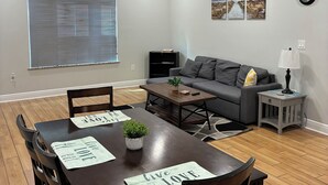 Ein modernes Wohnzimmer mit Esstisch, Sofa und einem großen Fenster mit Jalousien.