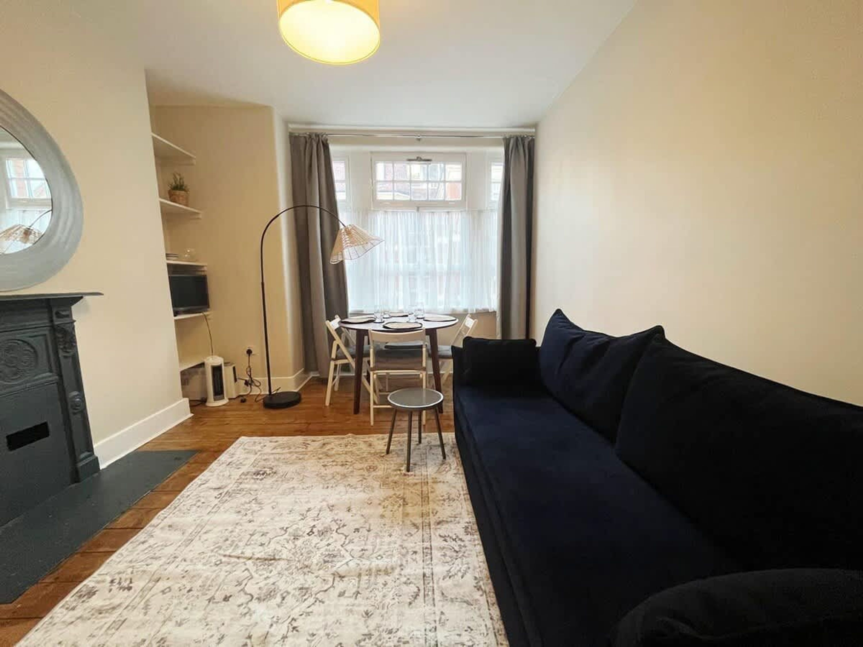 Ein Wohnzimmer mit einem dunkelblauen Sofa, einem runden Tisch mit Stühlen, einer Stehlampe und einem Kamin.