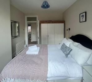Un dormitorio con cama, armario, espejo y puerta que da a otra habitación.