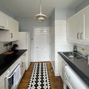 Una cocina estrecha con armarios blancos, encimera negra, piso estampado y puerta blanca.