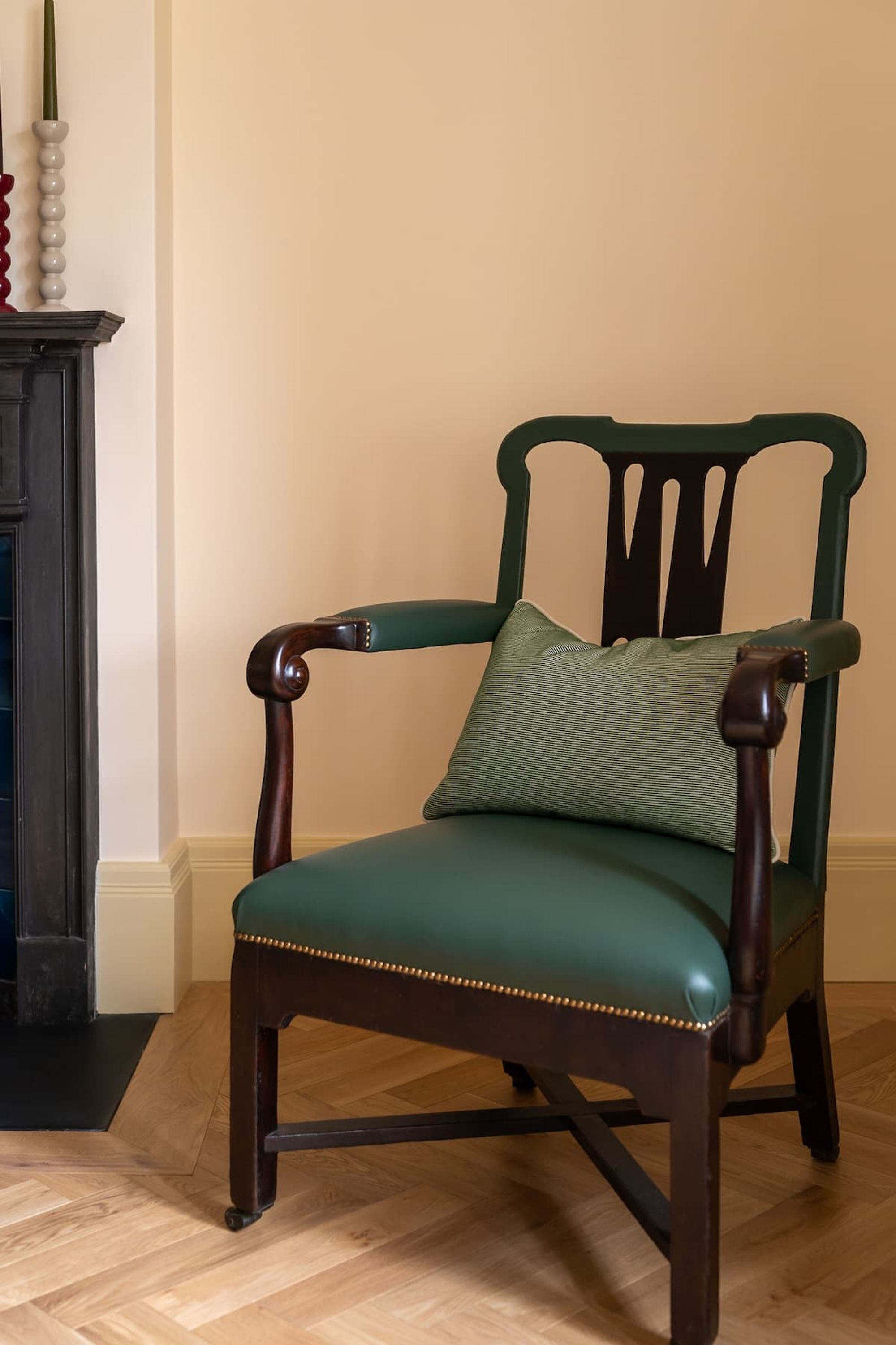 A dark wooden chair with a green cushion and a decorative pillow, positioned in a room with a wooden floor and a white wall.