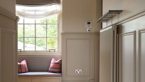 A hallway with a wooden herringbone floor, a window with striped blinds, a radiator, and a bench with cushions. - Melody Apartament in Greater London (London)