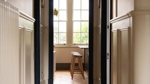 A hallway leading to a kitchen with a window, wooden stools, and a view of greenery outside. - Melody Apartament in Greater London (London)