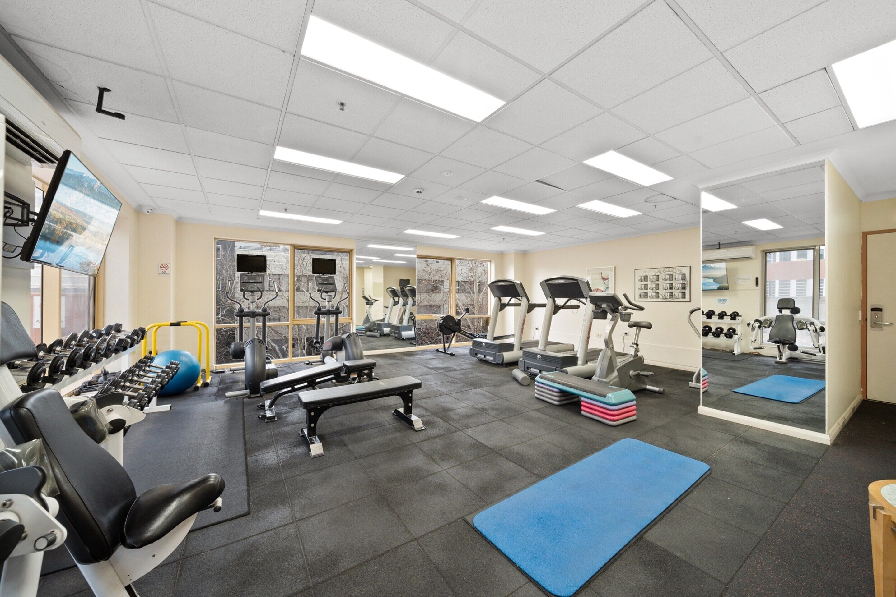 Une salle de sport équipée de divers appareils d’exercice, notamment des tapis de course, des appareils de musculation et des poids libres.
