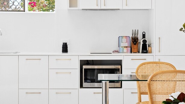 Een moderne keuken met witte kasten, een oven van roestvrij staal, en een eethoek met een ronde tafel en rieten stoelen.