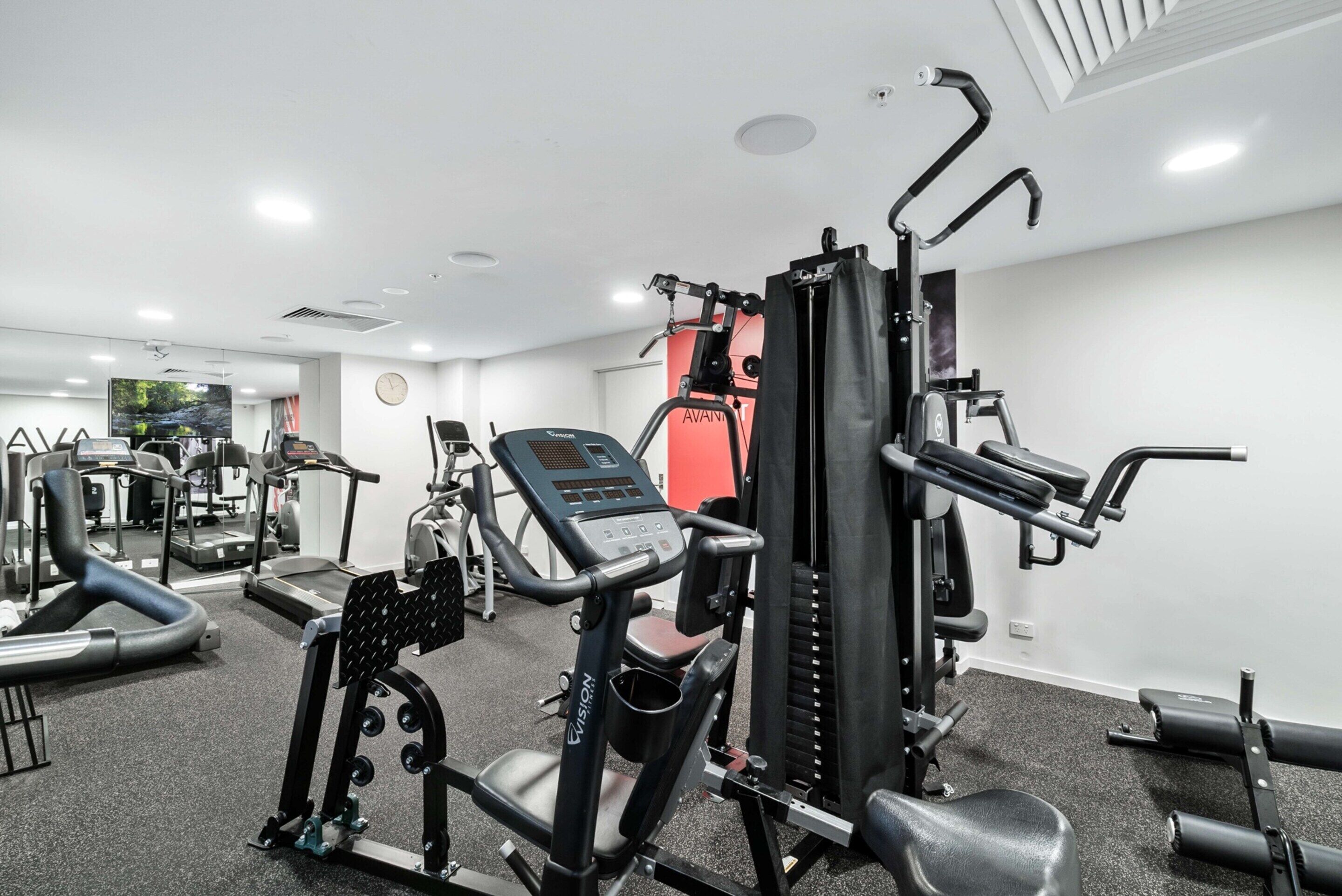A gym with various exercise machines, a treadmill, and a television screen.