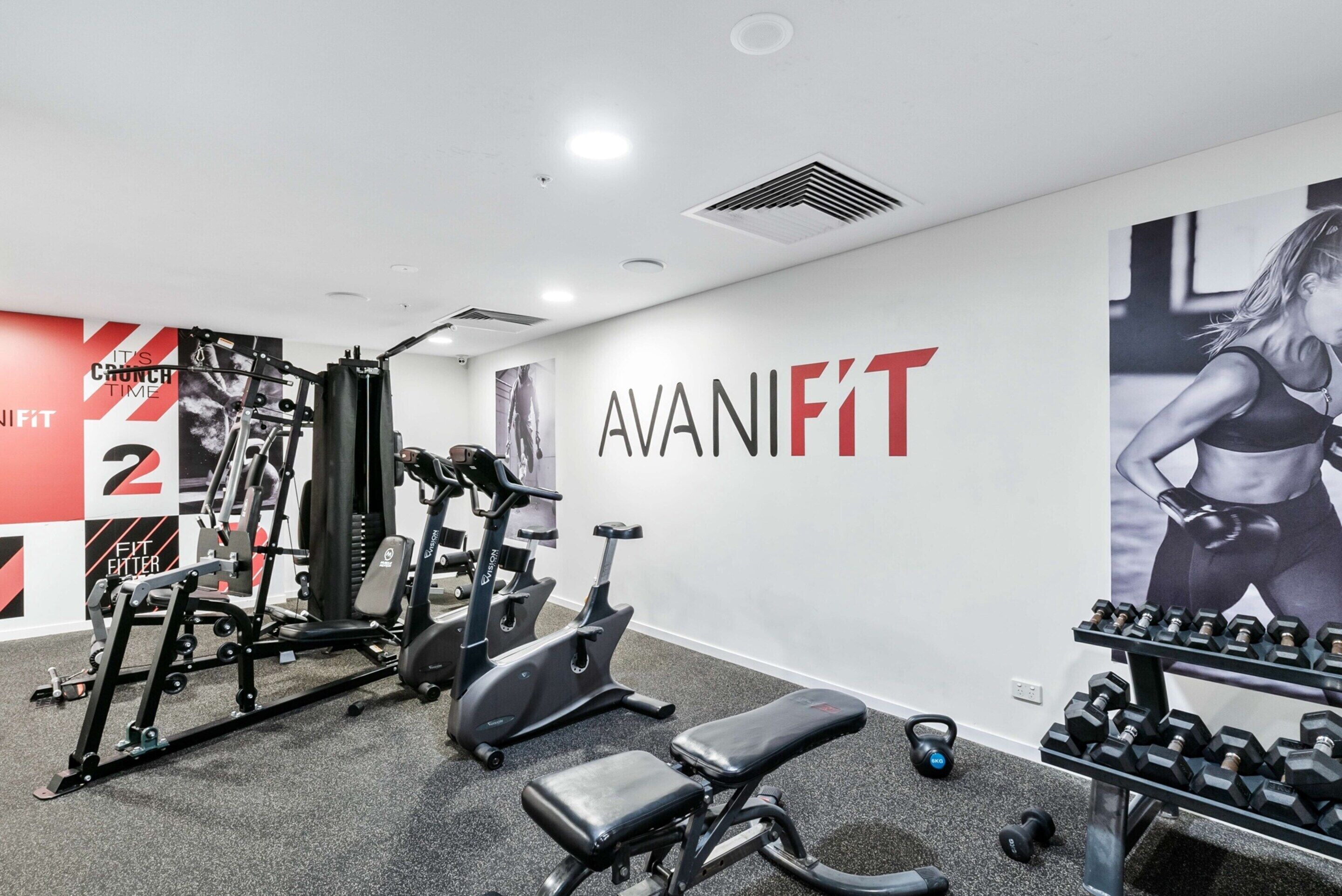 A gym with exercise equipment, a wall with 'AVANIFIT' branding, and a poster of a woman exercising.