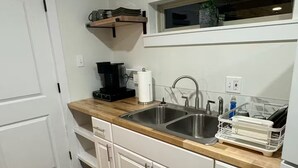 Eine kompakte Küche mit weißen Schränken, einer Holzarbeitsplatte, einer Edelstahlspüle und einer Kaffeemaschine.