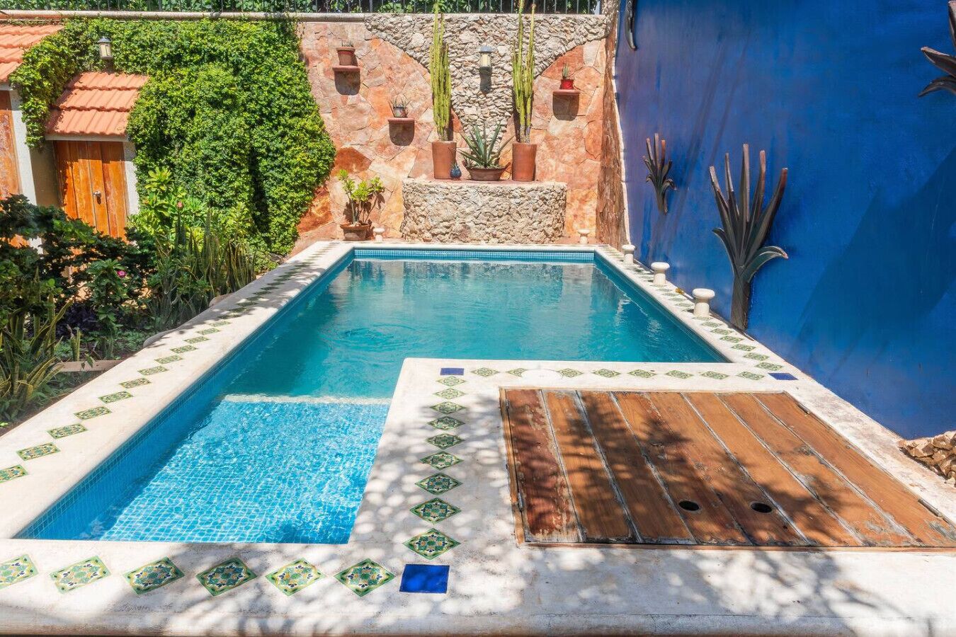 A rectangular swimming pool with a tiled edge, surrounded by a stone wall and a blue wall with decorative elements.