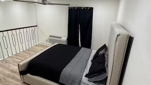 Un dormitori amb un llit, un ventilador de sostre, una finestra amb cortines i una barana blanca.