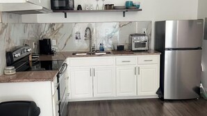 A modern kitchen with white cabinets, a stainless steel refrigerator, a microwave, a toaster, and a trash bin.