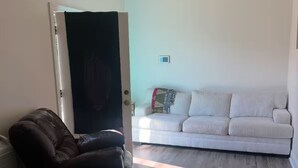 A living room with a dark leather sofa, a white couch, and a wooden floor.