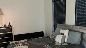 A bedroom with a large bed, a nightstand, and two windows with blinds.