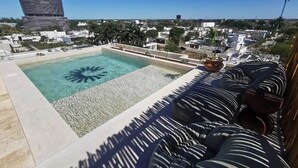 Ein Pool auf dem Dach mit Palmenmotiv, ein modernes Gebäude im Hintergrund und Blick auf die Stadtlandschaft.