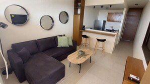 Ein modernes Wohnzimmer mit einem dunklen Sofa, einem Couchtisch und einer Küchenzeile mit einer Arbeitsplatte und Hockern.