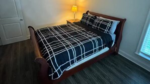 A bedroom with a bed, a ceiling fan, a nightstand with a lamp, and a window. - Frenchie Baker (Baker)