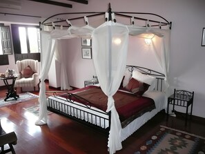 A four-poster canopy bed with a red bedspread, a chair, a small table with a bottle, and a patterned rug. - Country House 'Cortijo Puertoelperal' with Mountain View, Wi-Fi and Air Conditioning (Monterroso)
