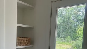 A narrow hallway with white walls, a trash bin, and a door leading to a garden.