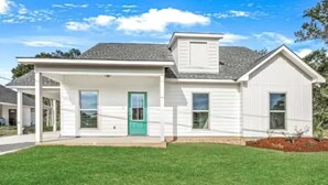 A single-story house with a front porch, a green door, and a sloped roof.