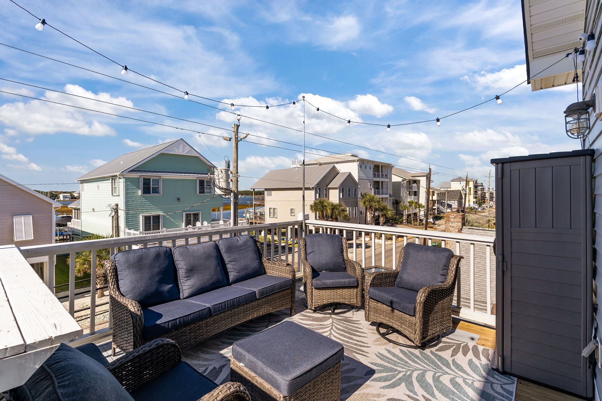 A balcony with wicker furniture, a white railing, and string lights.