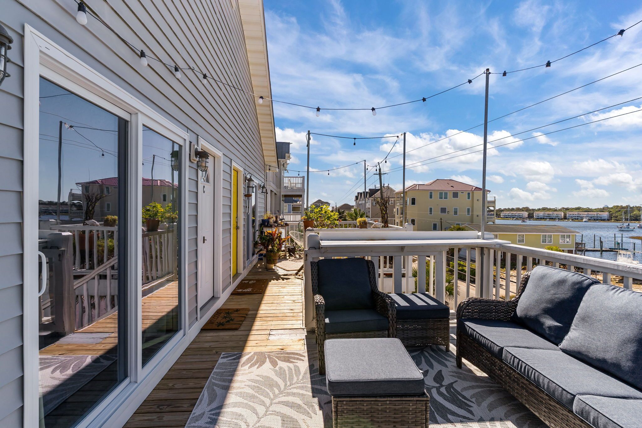 A wooden deck with outdoor furniture, a white railing, and a view of a body of water and buildings in the background.