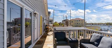 A wooden deck with outdoor furniture, a white railing, and a view of a body of water and buildings in the background.