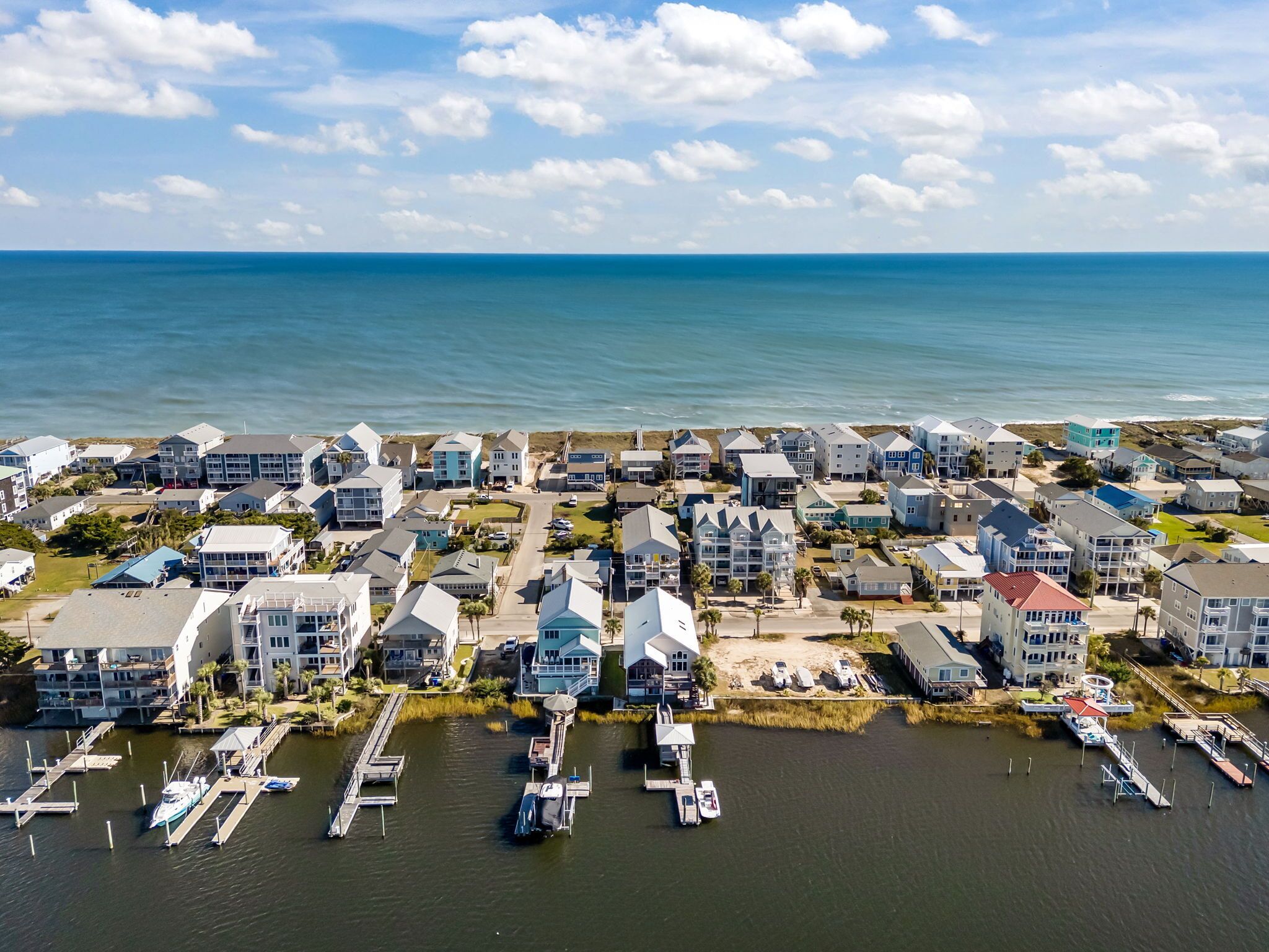 An aerial view of a coastal residential area with houses, a marina, and a clear view of the ocean.