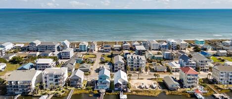 An aerial view of a coastal residential area with houses, a marina, and a clear view of the ocean.