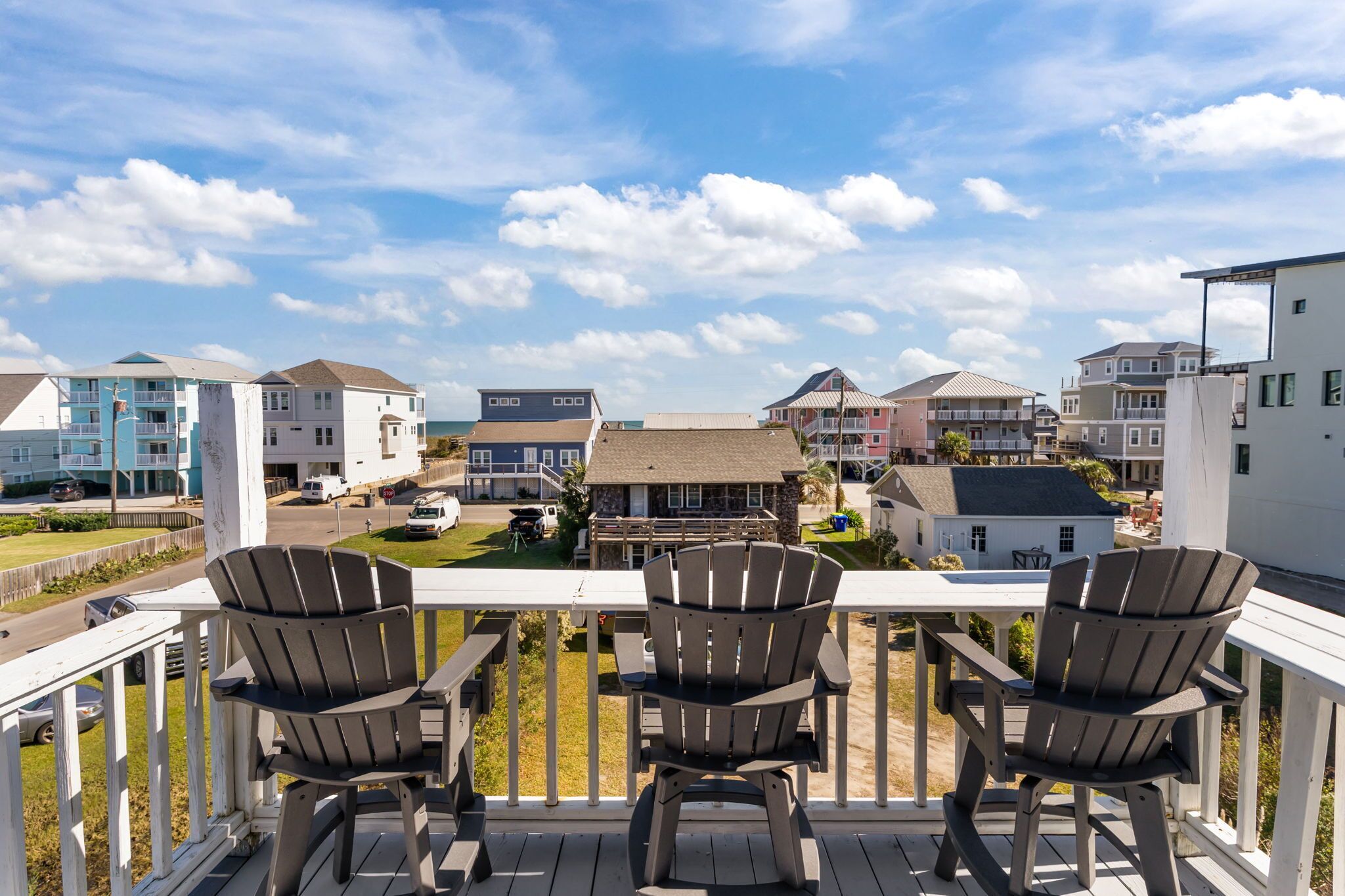 Un balcón con tres sillas Adirondack, con vista a una zona residencial con varias casas y un cielo despejado.