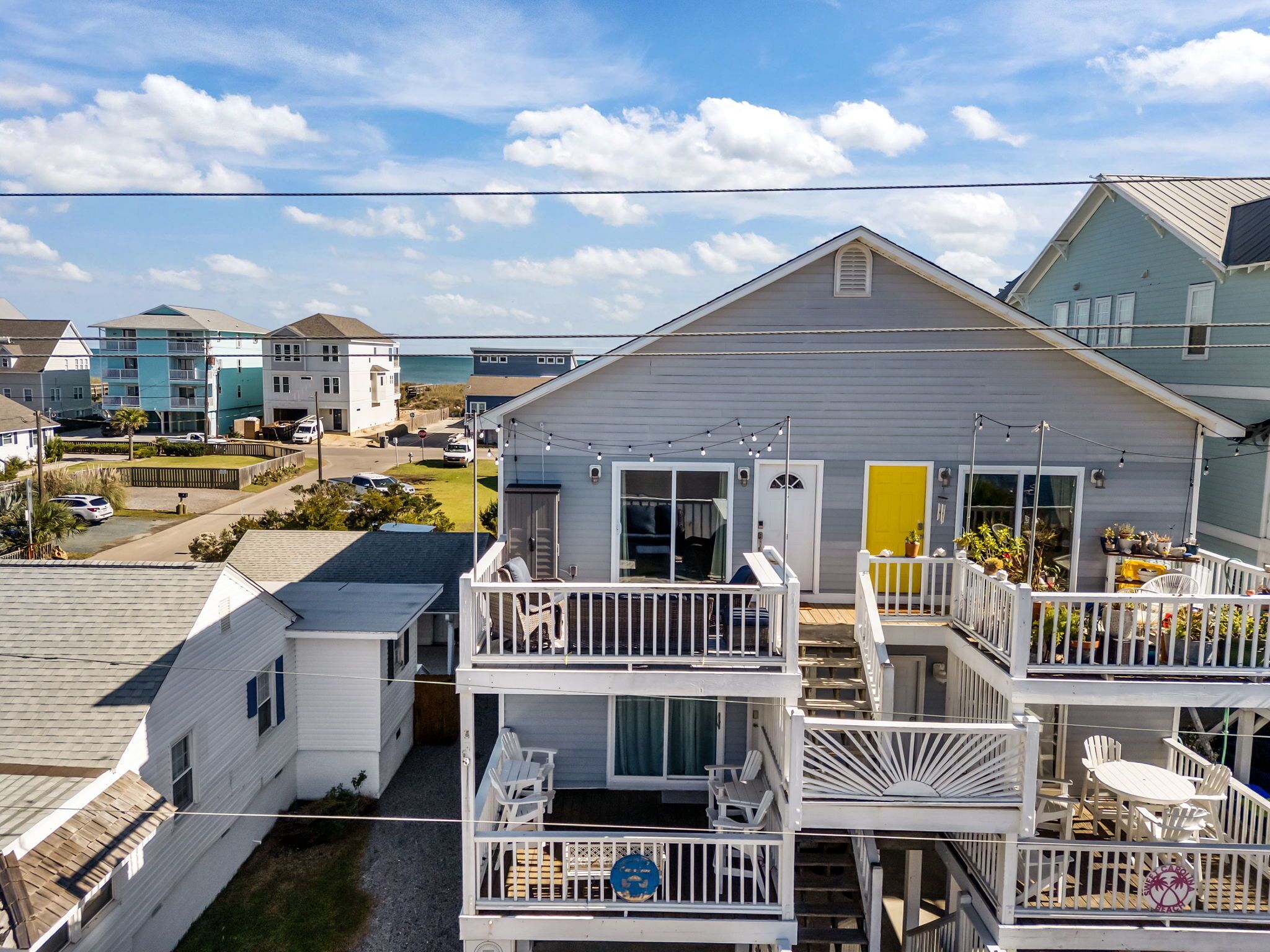 A multi-story house with a balcony, a yellow door, and a view of the ocean.