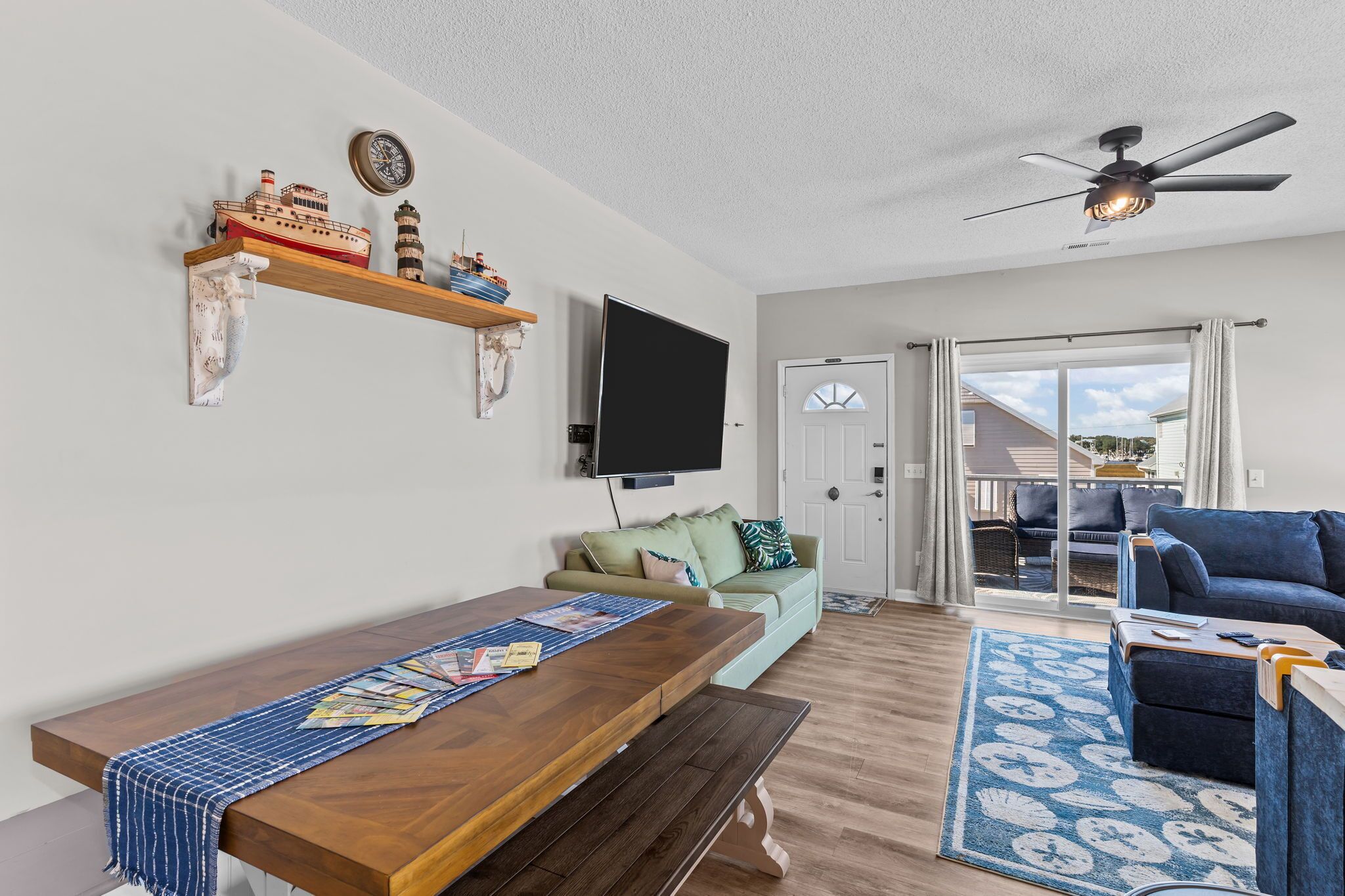 A living room with a wooden dining table, a green sofa, a blue couch, and a ceiling fan.