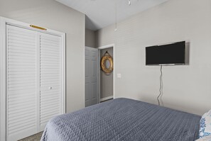 Un dormitorio con cama, armario blanco, puerta con sujetabroche para toallas y televisor en la pared.
