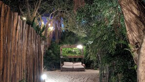 A pathway leading to a seating area with a bench and a canopy, surrounded by dense foliage and a wooden fence. - Luxury 4 Bedroom Villa, Private Pool Near to restaurants, cafes, bars & beach! (Tulum)