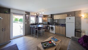 Een compacte keuken met een eethoek, geïntegreerde apparatuur en een schuifpui naar buiten.