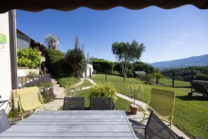 A patio with a table and chairs, a small garden with various plants, and a view of a mountain range. - Gîte le rêve: Between Lake and Mountains, Near Aix-les-Bains and Savoie Grand Revard (Viviers du Lac)
