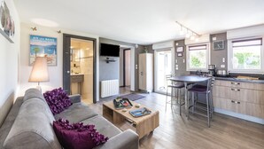 Een moderne woonkamer met een grijze bank, een houten salontafel en een keuken met een barstoel.
