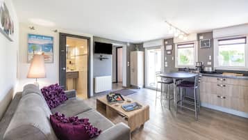 A modern living room with a grey sofa, a wooden coffee table, and a kitchen area with a bar stool.